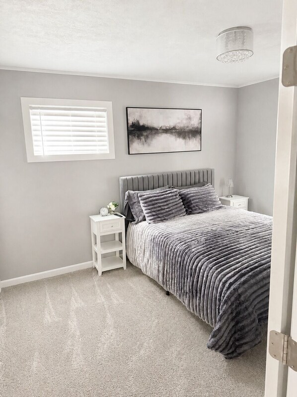 A bedroom with a bed, a nightstand, a wall-mounted picture, and a window with blinds. - NEW-Pictured Rocks Paradise!
Near Pictured Rocks & Lake Superior! (Shingleton)
