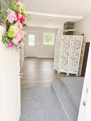 A hallway with a grey carpet, white walls, a white door, and a decorative white panel with leaf patterns.
