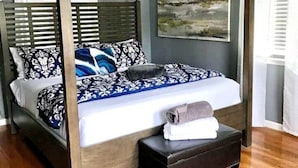A four-poster bed with a wooden frame, a white mattress, and patterned pillows.