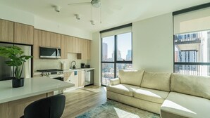 A modern kitchen with a built-in oven, microwave, and sink, a dining area with a black chair, and a large window offering a city view. - Saiya  1020 (Phoenix)
