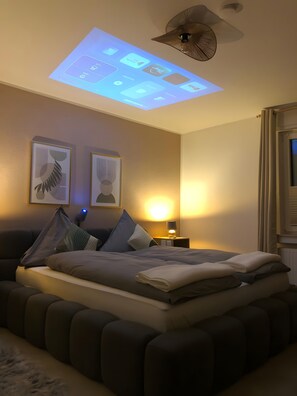 Camera da letto con un letto, cuscini, una lampada da comodino, un proiettore a soffitto e decorazioni alle pareti.