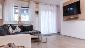 Un salon moderne avec un canapé, une table basse, un téléviseur fixé au mur et une fenêtre avec des rideaux.