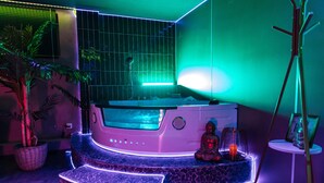Un espace détente avec un jacuzzi, quelques marches, une petite statue de Bouddha et un tableau encadré posé sur une table d’appoint.