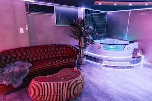 Ein modernes Interieur mit einem roten Ledersofa, einem runden Rattan-Hocker und einer Whirlwanne mit LED-Beleuchtung.