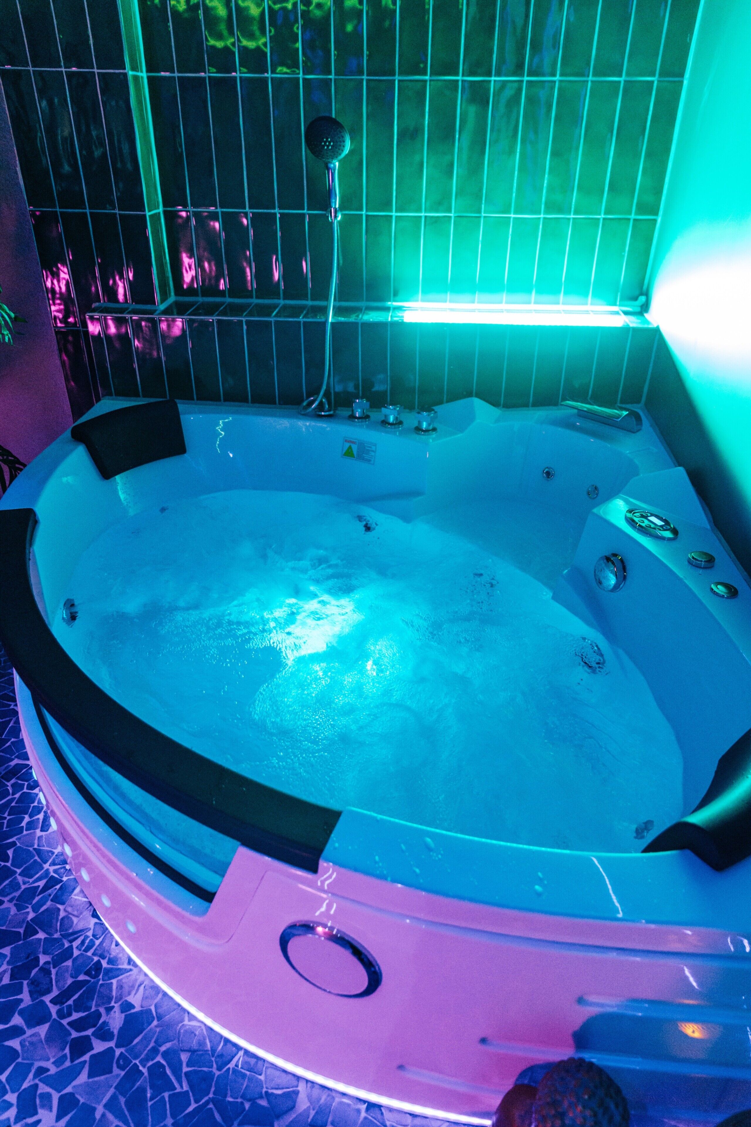 A hot tub with a tiled floor, a showerhead, and a control panel.