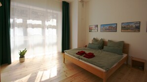 Ein Schlafzimmer mit einem hölzernen Bett, grünen Vorhängen, einem Blumentopf und zwei an der Wand befestigten Bildern.