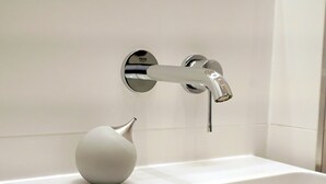 Ein Badezimmer mit einem modernen Wasserhahn, einem weißen Waschbecken und einer weißen Dekorvase.