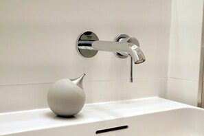 Ein Badezimmer mit einem modernen Wasserhahn, einem weißen Waschbecken und einer weißen Dekorvase.