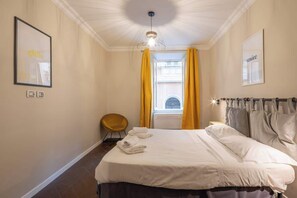 A hotel room with a bed, a chair, a window with yellow curtains, and a wall with framed pictures. - BuddyRent - Ghetto - Campo de' Fiori - 6 ospiti (Roma)