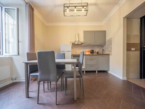A modern kitchen with grey cabinets, a stainless steel range hood, and a dining area with a table and chairs. - BuddyRent - Ghetto - Campo de' Fiori - 6 ospiti (Roma)