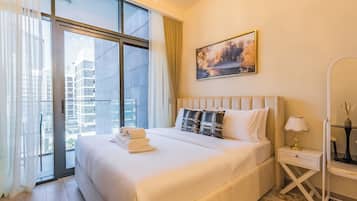 A modern hotel room with a large bed, a view of the city through floor-to-ceiling windows, a painting on the wall, and a bedside table with a lamp.