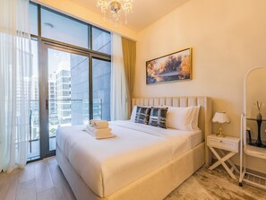 Ein modernes Hotelzimmer mit einem großen Bett, Blick auf die Stadt durch raumhohe Fenster, einem Bild an der Wand und einem Nachttisch mit Lampe.