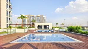 A rooftop pool area with a wooden deck, a swimming pool, and a building with multiple balconies in the background. - Tranquil Studio Getaway in Meydan City (Dubai)