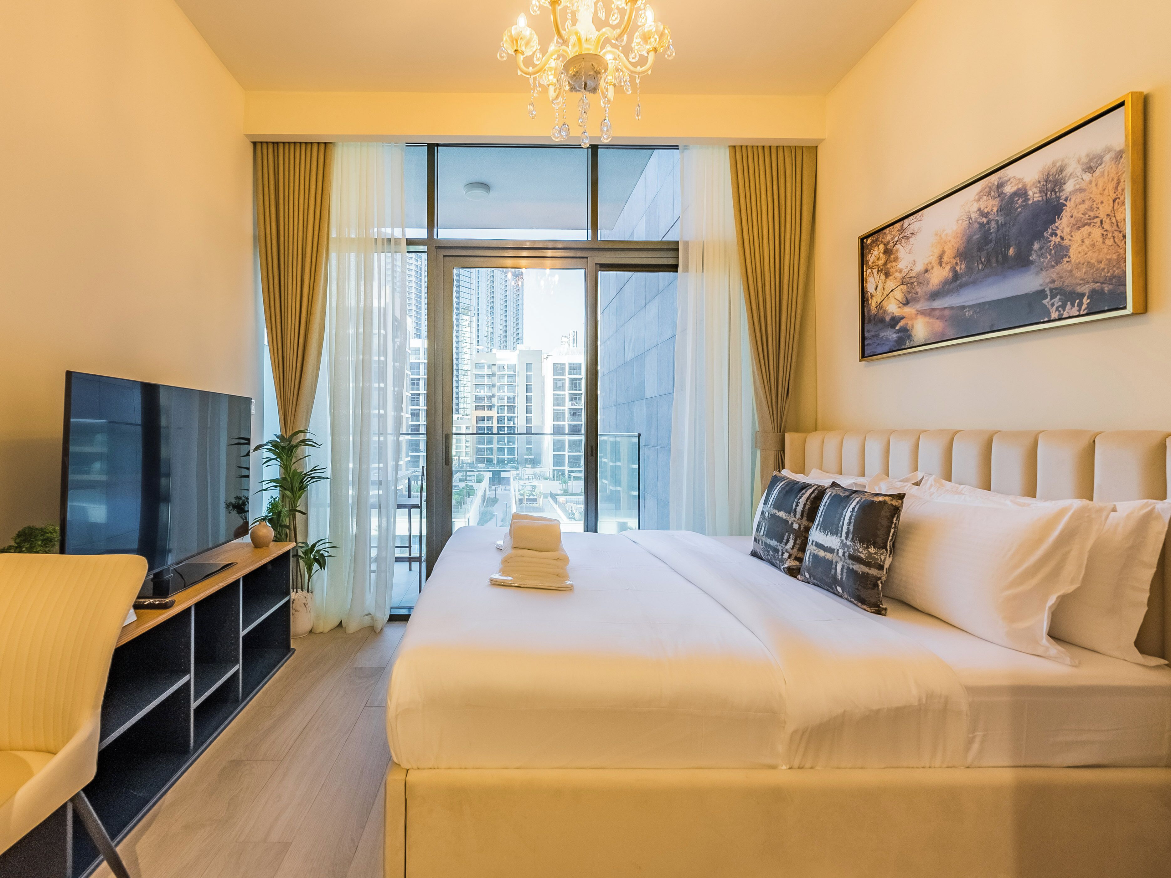 A hotel room with a large bed, a TV, a desk, and a window with curtains.