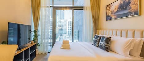 A hotel room with a large bed, a TV, a desk, and a window with curtains.