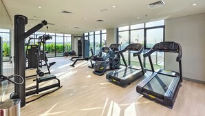 A modern gym with treadmills, weight machines, and a large window offering a view of greenery. - Tranquil Studio Getaway in Meydan City (Dubai)