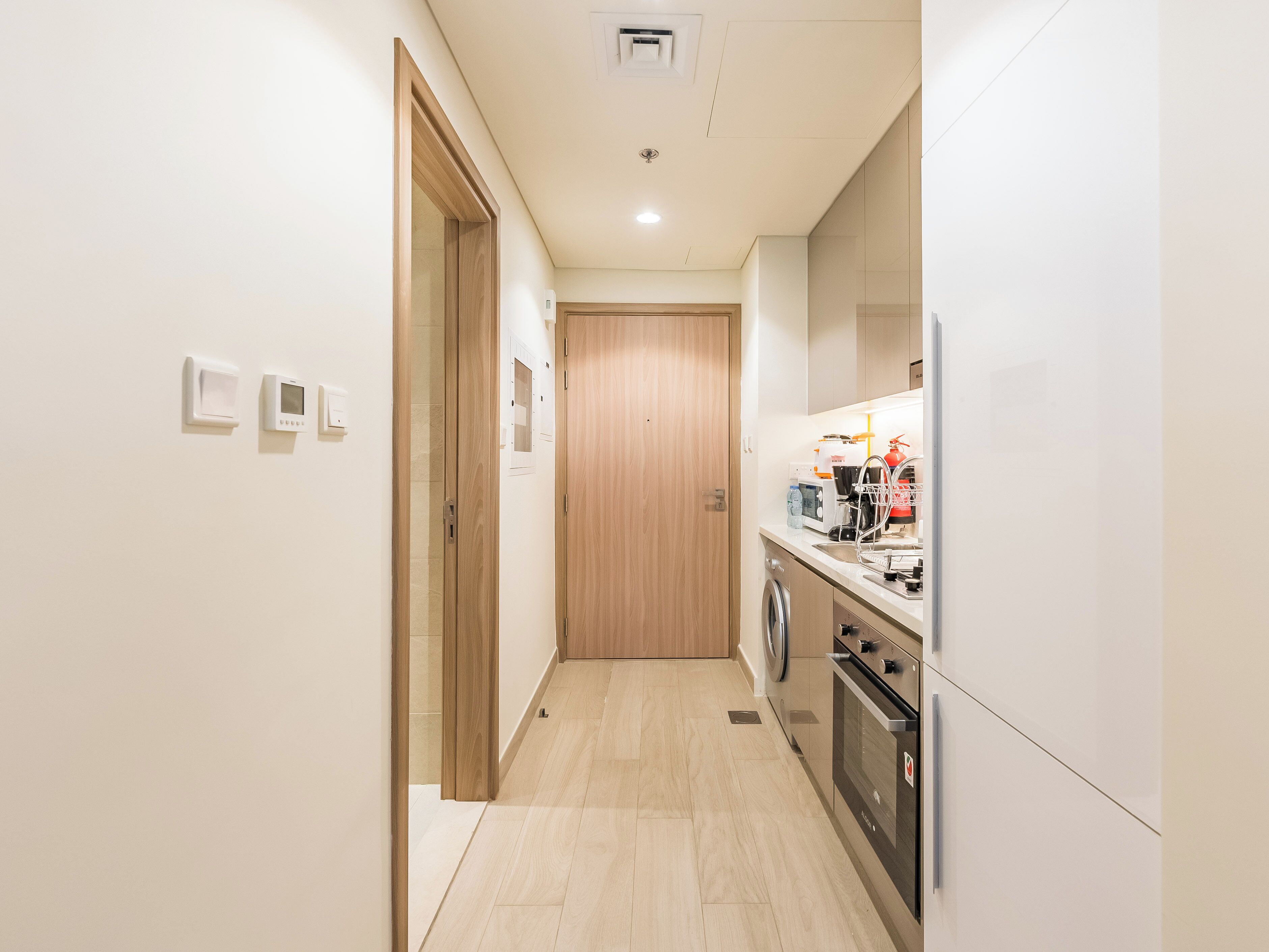 A narrow kitchen with a washing machine, oven, and a microwave on the counter.