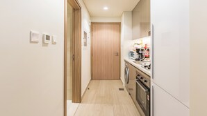 A narrow kitchen with a washing machine, oven, and a microwave on the counter. - Tranquil Studio Getaway in Meydan City (Dubai)