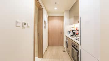 A narrow kitchen with a washing machine, oven, and a microwave on the counter.