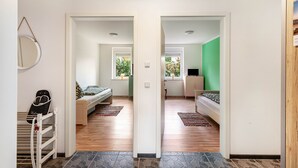 Un couloir mène à une chambre qui contient un lit, une commode et une fenêtre donnant sur un paysage verdoyant.