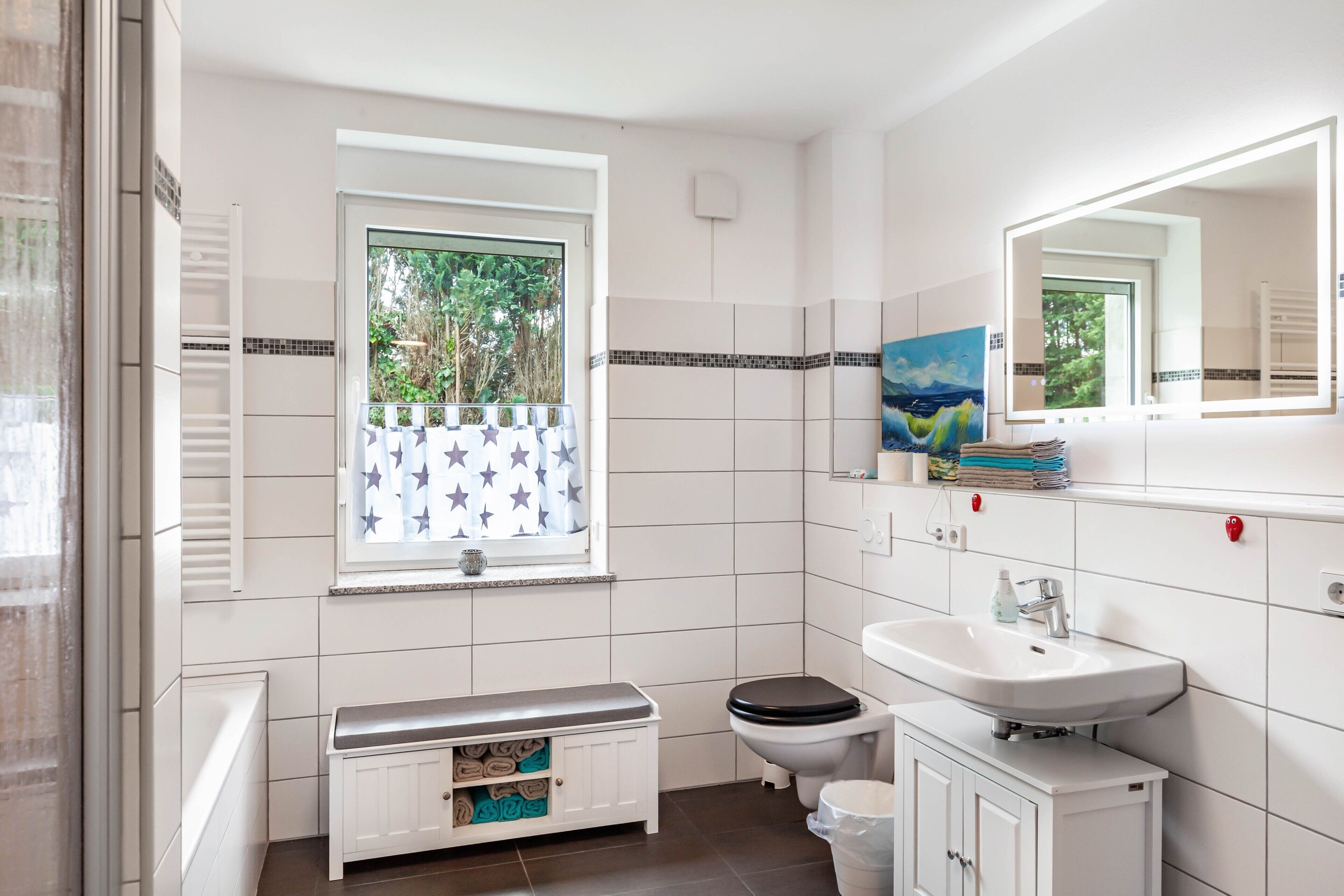 Ein Badezimmer mit Toilette, Waschbecken, Fenster mit Vorhang mit Sternenmuster und einer Bank mit Handtüchern.