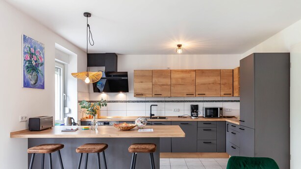 Une cuisine moderne avec des meubles en bois, un îlot central doté de tabourets, un four à micro-ondes et une machine à café.