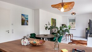 Un coin repas avec une table en bois, un vase contenant des feuilles vertes, un panier de biscuits et un livre aux couleurs vives.