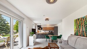 Un intérieur moderne comprenant un canapé, une table à manger et des chaises, un coin cuisine et une grande fenêtre donnant sur un paysage verdoyant.