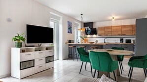 Une cuisine moderne dotée d’un téléviseur à écran plat, de meubles en bois et d’un coin repas avec des chaises vertes.