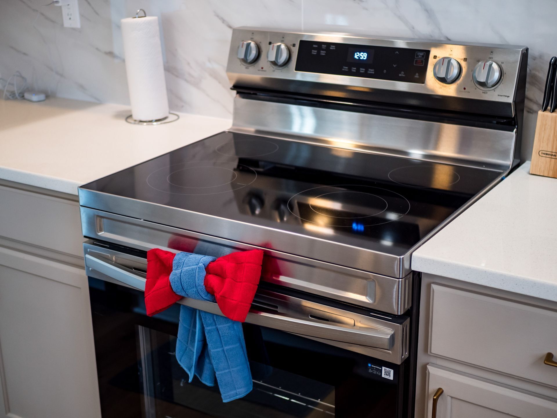 A stainless steel oven with a digital clock, a red and blue towel, and a marble backsplash.