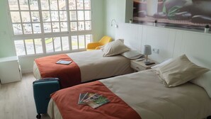 Habitació d'hotel amb dos llits, una finestra que dona al carrer, una cadira i una maleta.