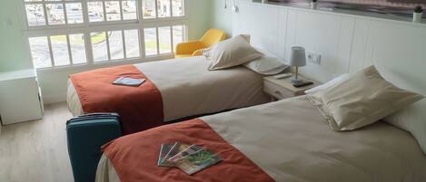 A hotel room with two beds, a window with a view of the street, a chair, and a suitcase.