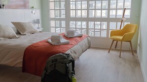 Una habitació d'hotel amb un llit, una cadira groga i una finestra que dona al paisatge exterior.