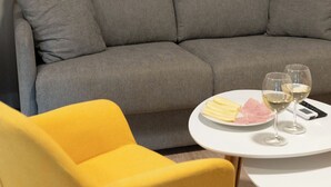 Un sofà gris, una cadira groga i una taula petita amb gots i un plat de menjar.