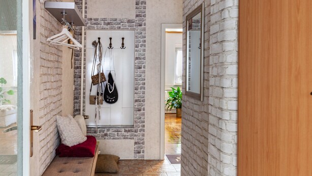 A hallway with a brick wall, a bench with cushions, a coat rack, and a mirror.