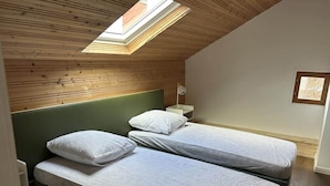 A room with two beds, a skylight, and a small bedside table with a lamp. - Les Coteaux III (Gérardmer)