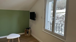 A room with a large window, a television mounted on the wall, and a small table. - Les Coteaux III (Gérardmer)