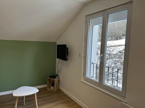 A room with a large window, a television mounted on the wall, and a small table. - Les Coteaux III (Gérardmer)