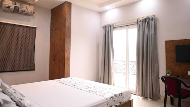 Une chambre à coucher avec un lit, une armoire en bois, un bureau avec une chaise, une fenêtre avec des rideaux et un téléviseur fixé au mur.