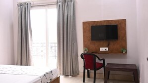Une chambre à coucher comprenant un lit, un bureau, une chaise, un téléviseur fixé au mur et un ventilateur de plafond.