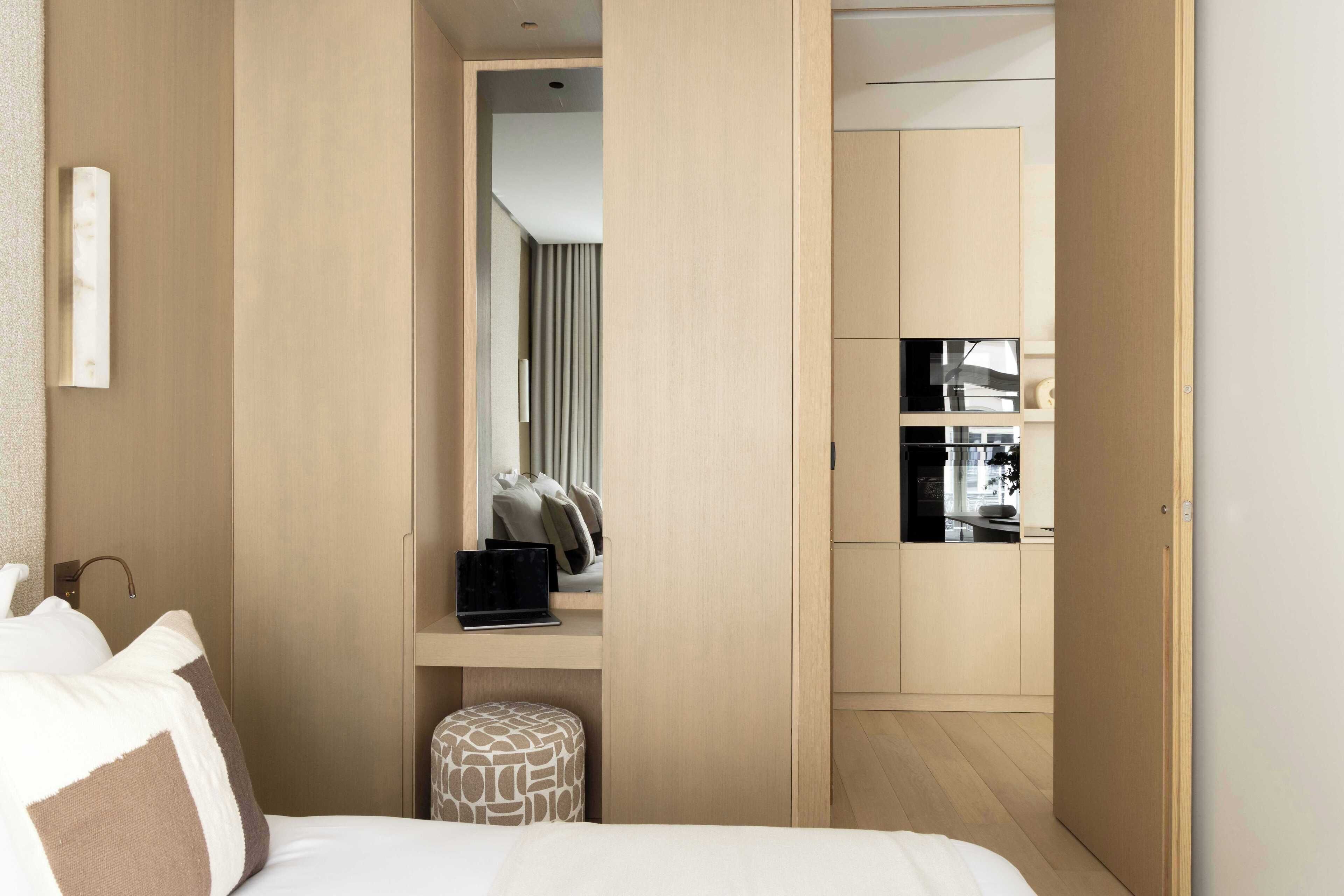 Ein Hotelzimmer mit einem Bett, einem Schreibtisch mit einem Laptop, einem kleinen Hocker und einem Kleiderschrank.
