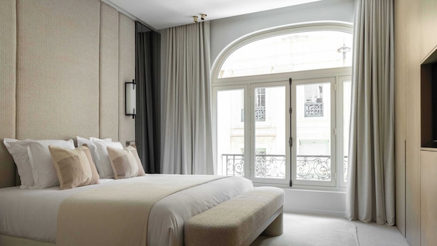 A bedroom with a large bed, a bench, a window with curtains, and a view of the outside. - Luxurious Astorg Residence (Paris)