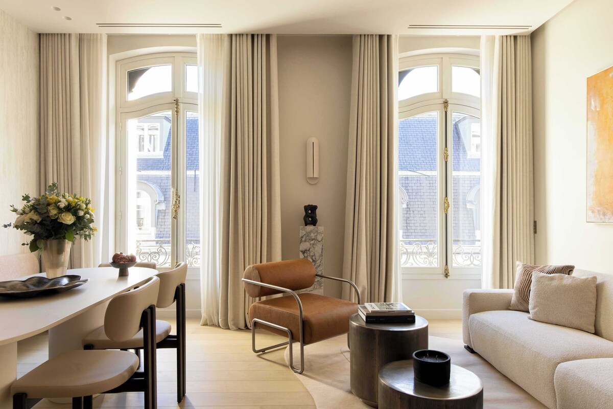 A modern living room with a sofa, a dining table with chairs, a coffee table, and a window with curtains.