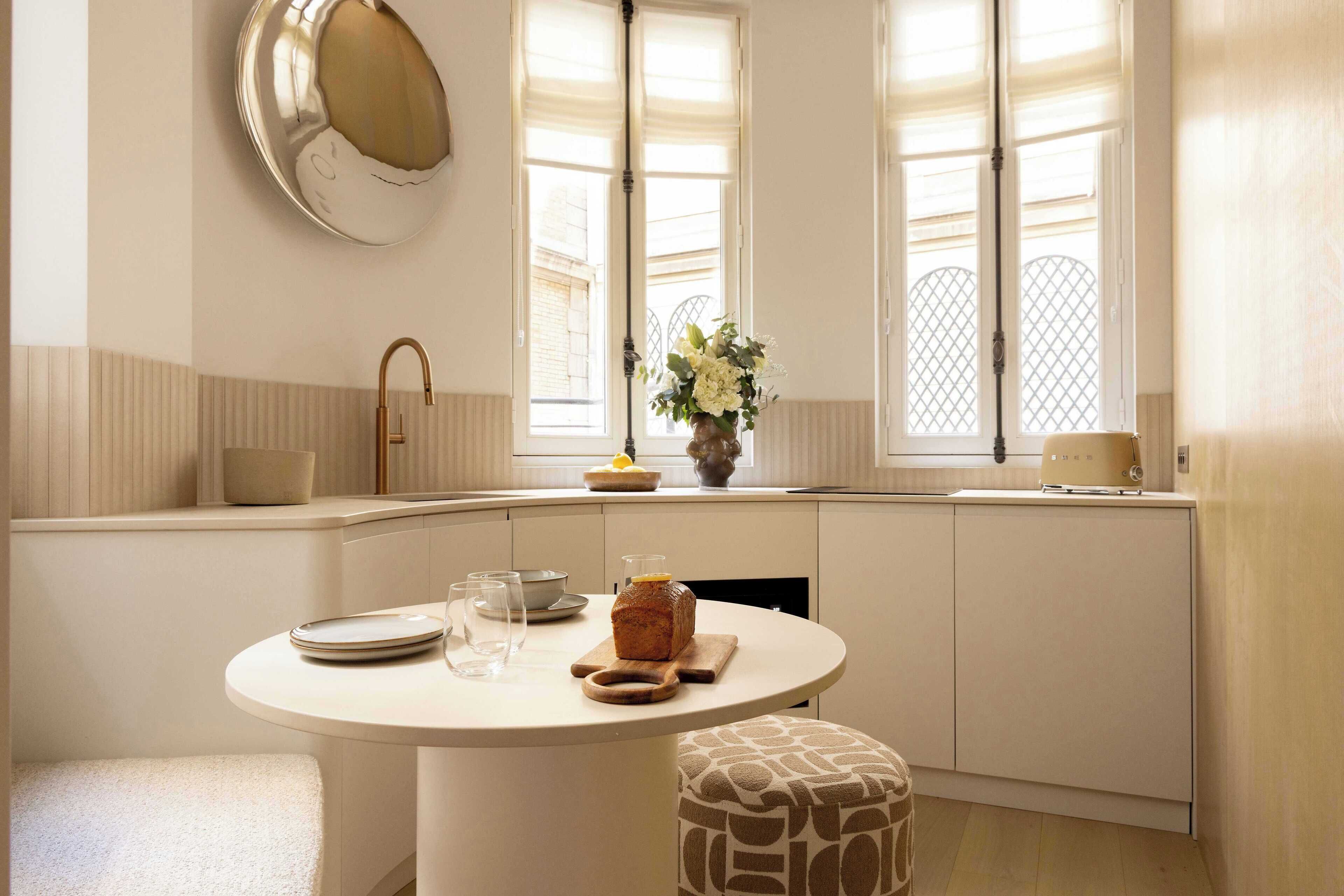 A modern kitchen with a round dining table, a built-in oven, and a window with a view.