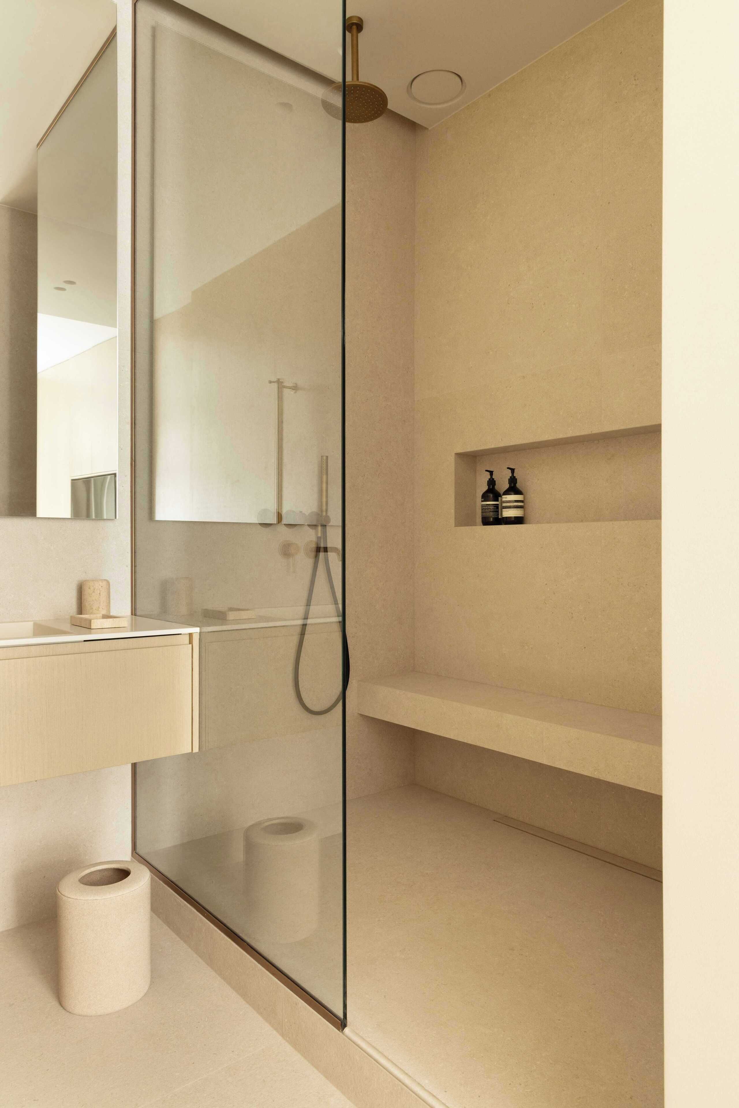 Un baño moderno con cabina de ducha de vidrio, tocador de madera y un estante pequeño con artículos de aseo.