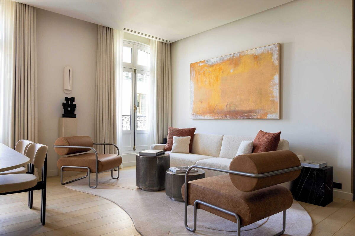 A modern living room with a sofa, armchairs, a coffee table, and a large abstract painting on the wall.
