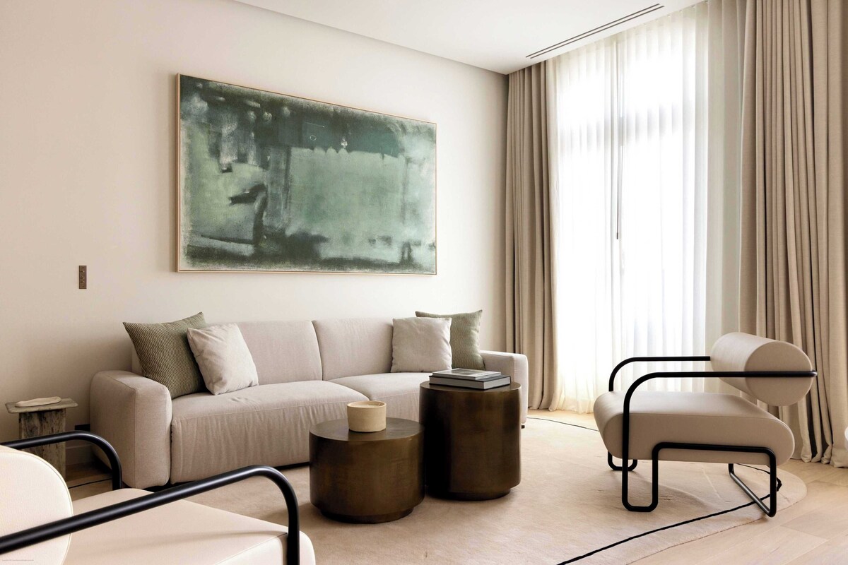 A modern living room with a sofa, two side tables, a chair, and a large abstract painting on the wall.