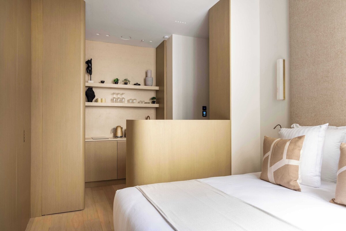 A modern hotel room with a bed, bedside table, and a built-in desk with shelves.