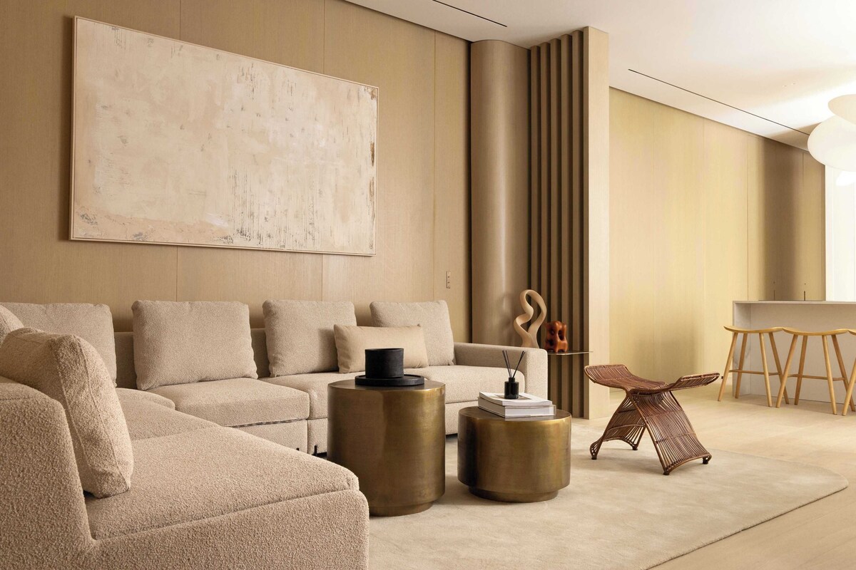 A modern living room with a sectional sofa, two round side tables, a coffee table, a decorative chair, and a large abstract painting on the wall.