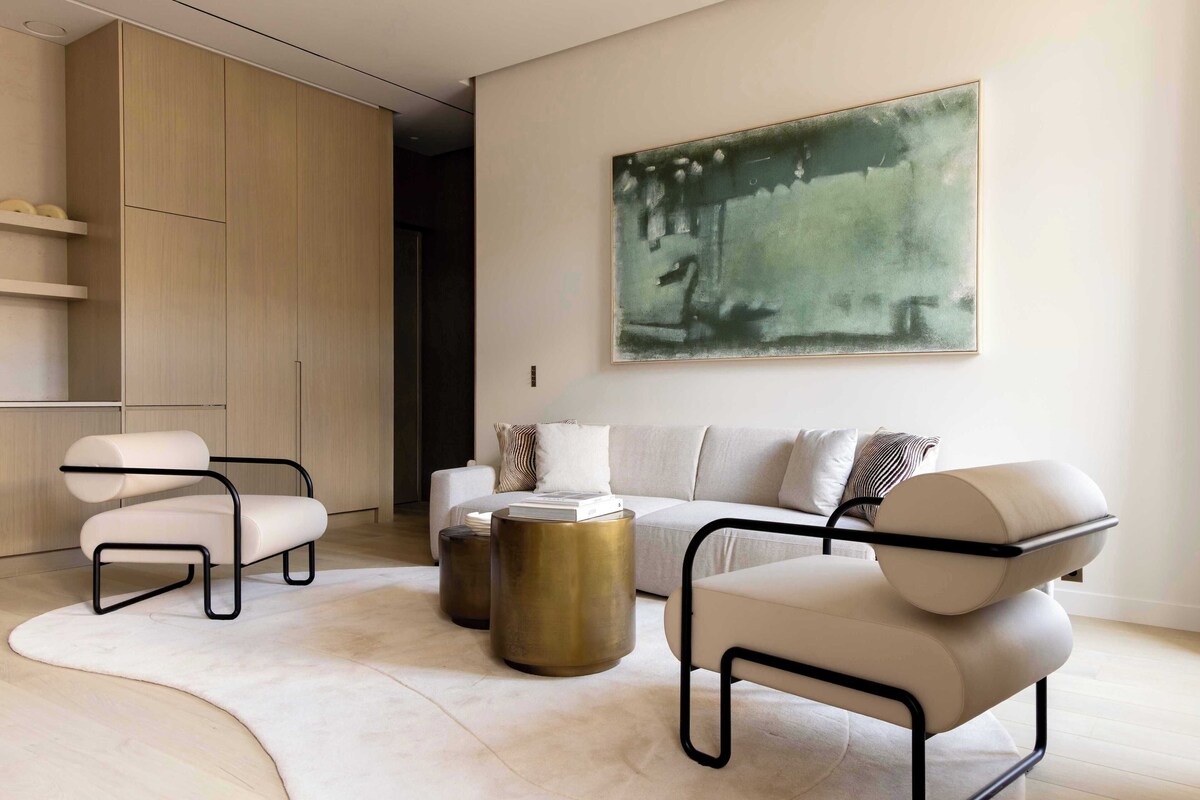 A modern living room with a sofa, two armchairs, a coffee table, and a large abstract painting on the wall.